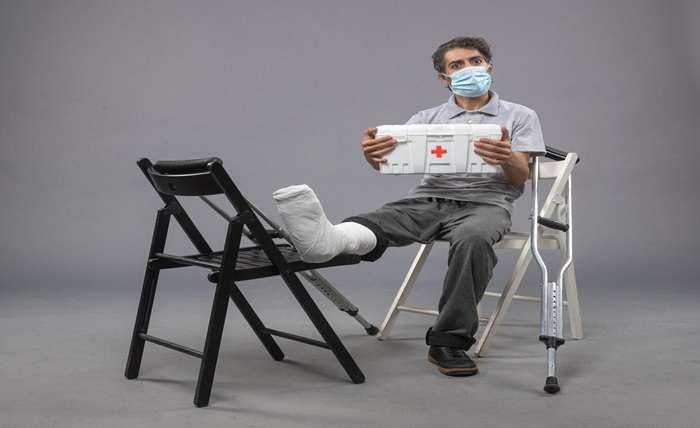 front view young male wearing mask sitting with bandaged broken foot grey wall twist male broke legs pain foot 140725 116397